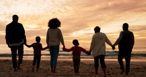 Multigenerational family holding hands on the beach at sunset, symbolizing legacy, connection, and generational wealth.